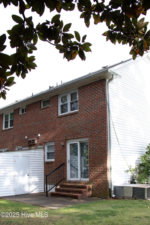 rear view of house featuring central air condition unit, entry steps, a yard, and brick siding