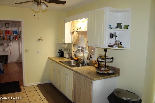 kitchen featuring light tile patterned floors, baseboards, a sink, ceiling fan, and white cabinetry