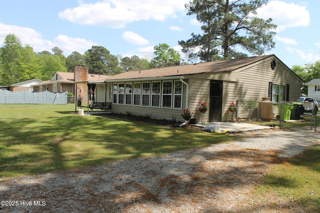 back of property featuring a sunroom, a chimney, fence, and a lawn
