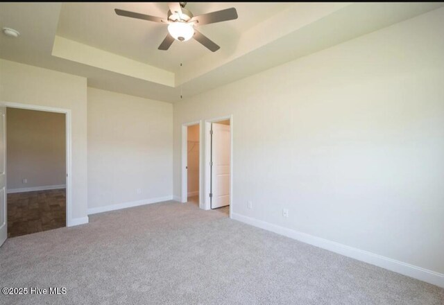 unfurnished bedroom featuring baseboards, a spacious closet, a raised ceiling, ceiling fan, and carpet