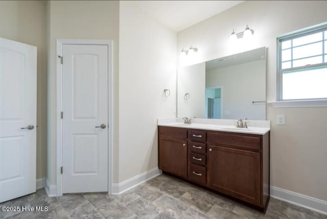 full bath with a sink, baseboards, double vanity, and stone finish floor