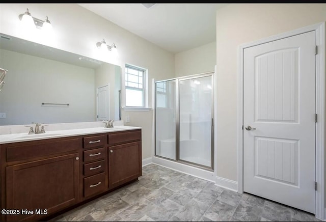bathroom with a shower stall, double vanity, baseboards, and a sink