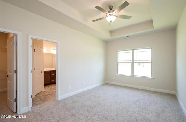 unfurnished bedroom with a raised ceiling, light carpet, baseboards, and a walk in closet