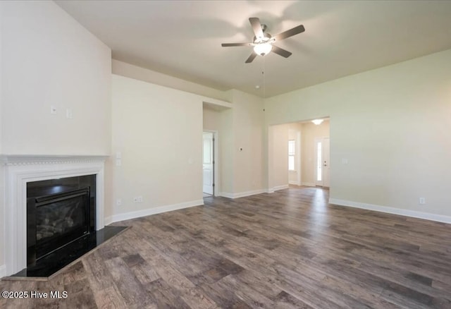 unfurnished living room featuring a glass covered fireplace, baseboards, wood finished floors, and ceiling fan