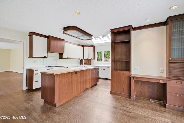 kitchen with open shelves, a sink, light countertops, dark wood-style floors, and a skylight