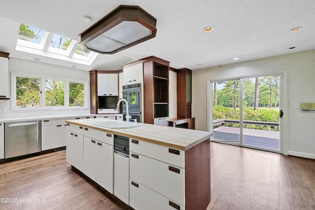 kitchen featuring open shelves, stainless steel dishwasher, white cabinets, light wood finished floors, and a skylight