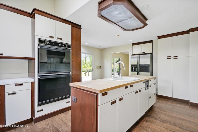 kitchen with butcher block countertops, a sink, dobule oven black, wood finished floors, and stainless steel fridge with ice dispenser