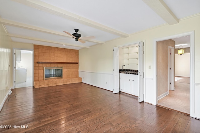 unfurnished living room featuring dark wood-style flooring, a ceiling fan, a tile fireplace, and beamed ceiling