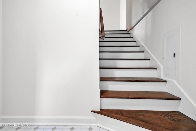 stairway featuring baseboards and electric panel
