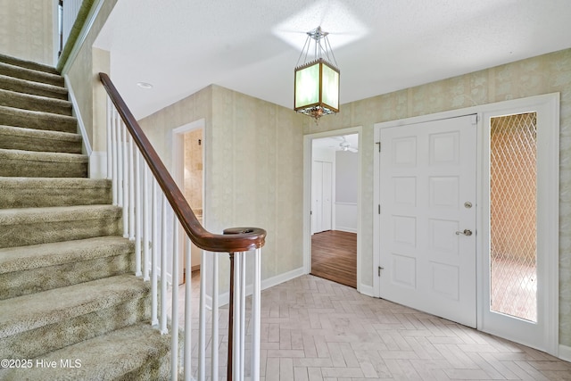 foyer entrance featuring stairway, ceiling fan with notable chandelier, brick floor, and baseboards