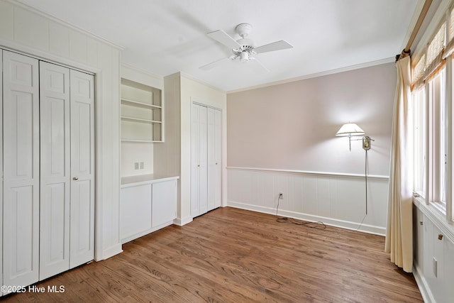 unfurnished bedroom featuring wood finished floors, multiple closets, crown molding, and a ceiling fan