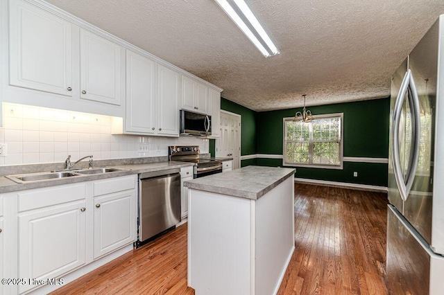 kitchen with a textured ceiling, white cabinets, a sink, stainless steel appliances, and hardwood / wood-style flooring