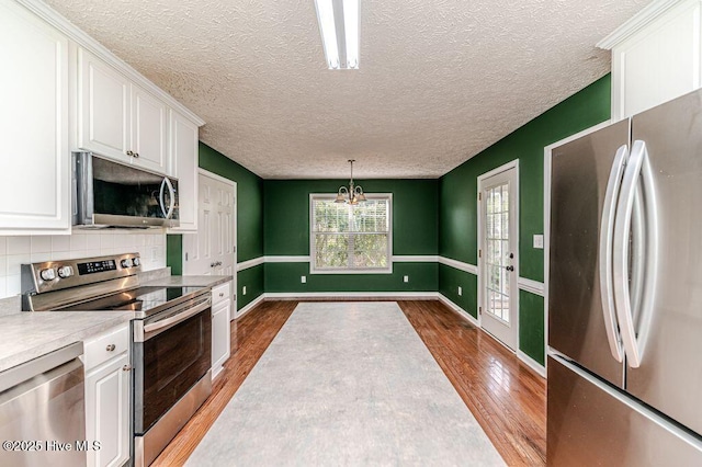 kitchen with baseboards, light countertops, white cabinetry, wood finished floors, and stainless steel appliances