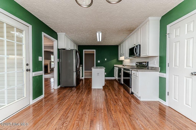 kitchen with a textured ceiling, white cabinets, wood finished floors, stainless steel appliances, and baseboards