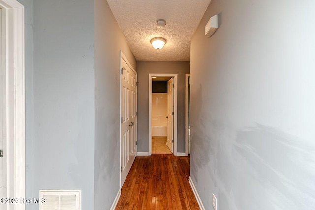 hallway with visible vents, a textured ceiling, baseboards, and wood finished floors