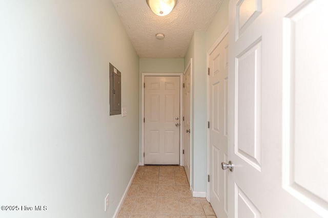 hallway featuring baseboards, light tile patterned flooring, electric panel, and a textured ceiling