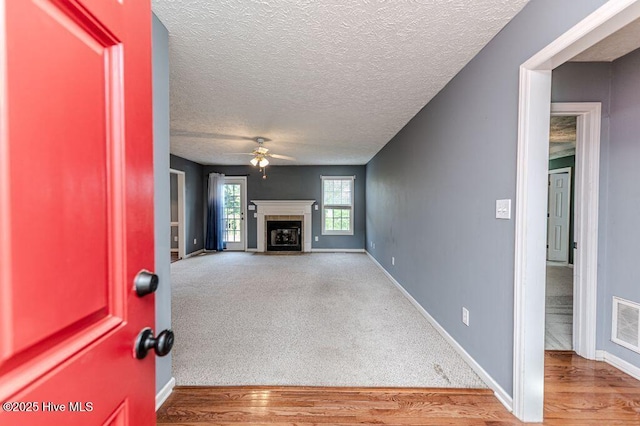 unfurnished living room featuring a tiled fireplace, ceiling fan, baseboards, and a textured ceiling