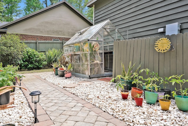 view of patio featuring fence, a greenhouse, and an outdoor structure
