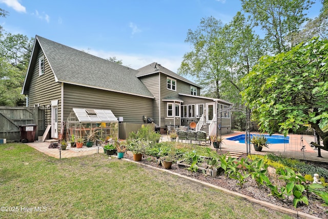 back of property featuring roof with shingles, a sunroom, a greenhouse, a patio area, and a yard