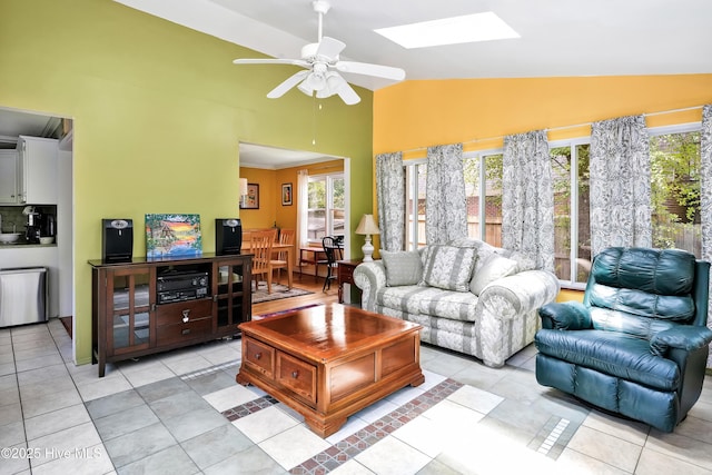 living area featuring a skylight, high vaulted ceiling, light tile patterned floors, and a ceiling fan