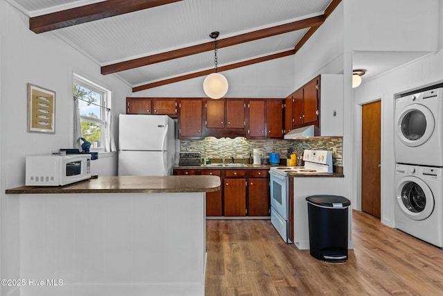 kitchen with stacked washer and dryer, a sink, dark countertops, lofted ceiling with beams, and white appliances