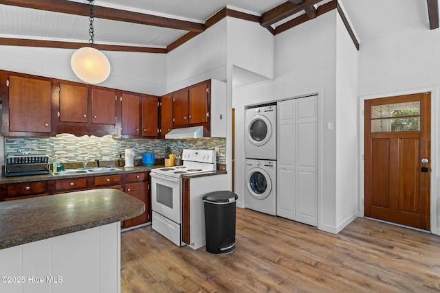 kitchen with a sink, stacked washing maching and dryer, backsplash, dark countertops, and electric range