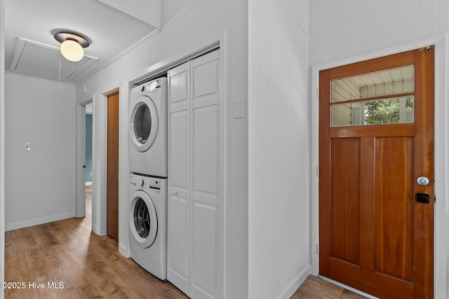 washroom with wood finished floors, laundry area, stacked washer / dryer, attic access, and baseboards