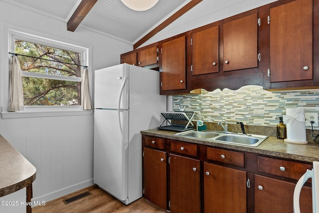kitchen with light wood finished floors, a sink, vaulted ceiling with beams, visible vents, and backsplash