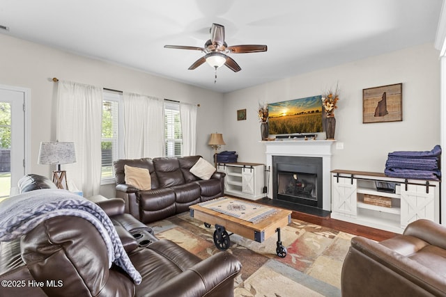 living area with wood finished floors, ceiling fan, a fireplace, and visible vents