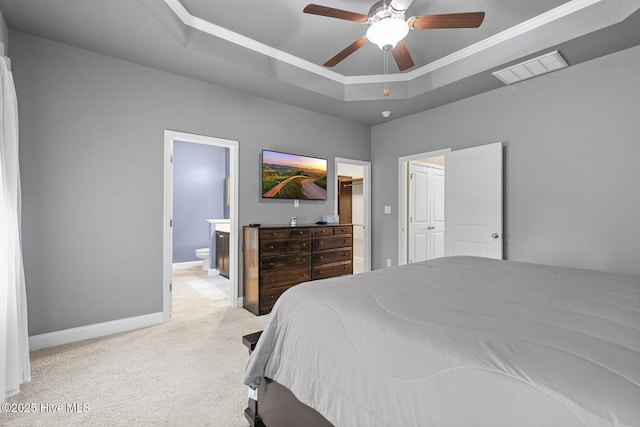 bedroom featuring visible vents, baseboards, a tray ceiling, ensuite bath, and carpet flooring