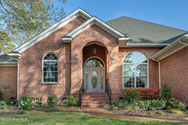 view of exterior entry featuring a shingled roof and brick siding
