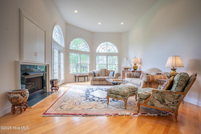 living area with recessed lighting, wood finished floors, a high ceiling, a premium fireplace, and baseboards