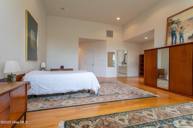 bedroom featuring connected bathroom, visible vents, recessed lighting, wood finished floors, and a high ceiling