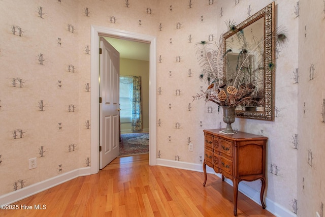 hall featuring light wood finished floors, baseboards, and wallpapered walls