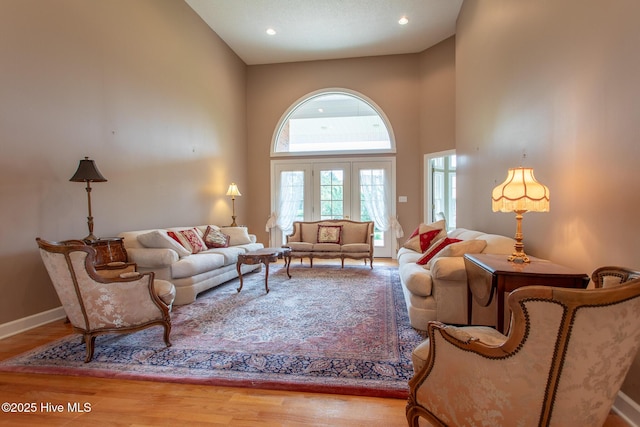 living area featuring recessed lighting, a towering ceiling, baseboards, and wood finished floors