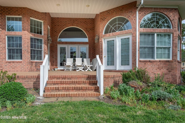 doorway to property with brick siding, a porch, and french doors