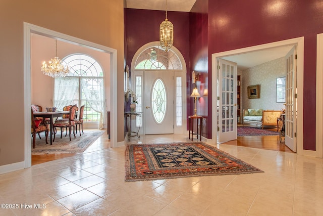 foyer entrance featuring french doors, an inviting chandelier, a towering ceiling, and baseboards