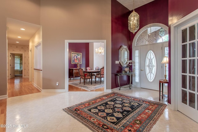tiled entryway with a towering ceiling, baseboards, and a notable chandelier