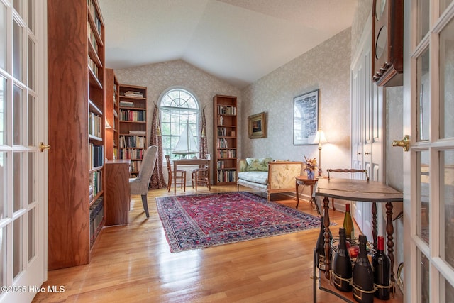 living area with french doors, wallpapered walls, wood finished floors, and vaulted ceiling