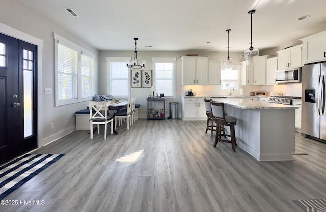 kitchen with stainless steel appliances, visible vents, light wood-style flooring, a center island, and baseboards