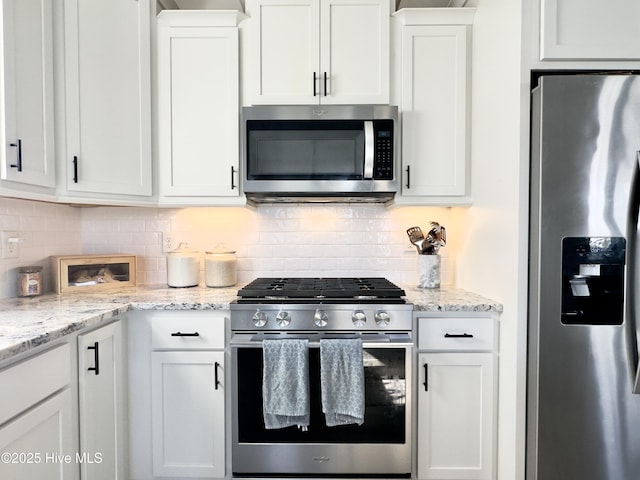 kitchen with stainless steel appliances, tasteful backsplash, light stone counters, and white cabinets