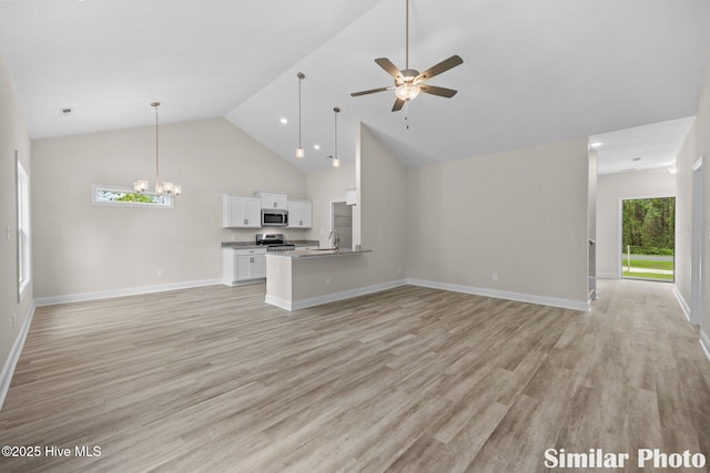 unfurnished living room featuring a sink, light wood-type flooring, high vaulted ceiling, and ceiling fan with notable chandelier