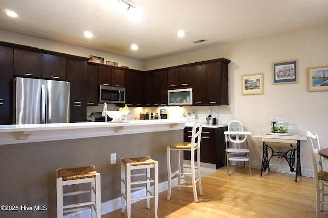kitchen with a breakfast bar area, light wood-style flooring, appliances with stainless steel finishes, dark brown cabinets, and light countertops