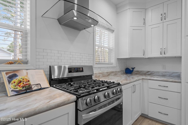 kitchen featuring white cabinets, stainless steel gas range, wall chimney exhaust hood, and backsplash