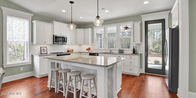 kitchen featuring a kitchen breakfast bar, white cabinets, visible vents, stainless steel appliances, and a kitchen island