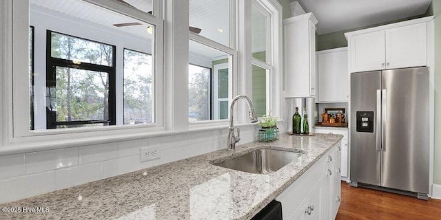 kitchen with white cabinetry, stainless steel fridge, backsplash, and a sink