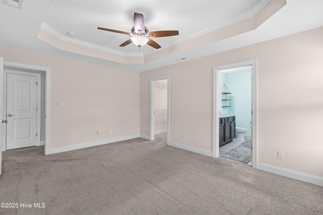 unfurnished bedroom with crown molding, a tray ceiling, light carpet, and a walk in closet