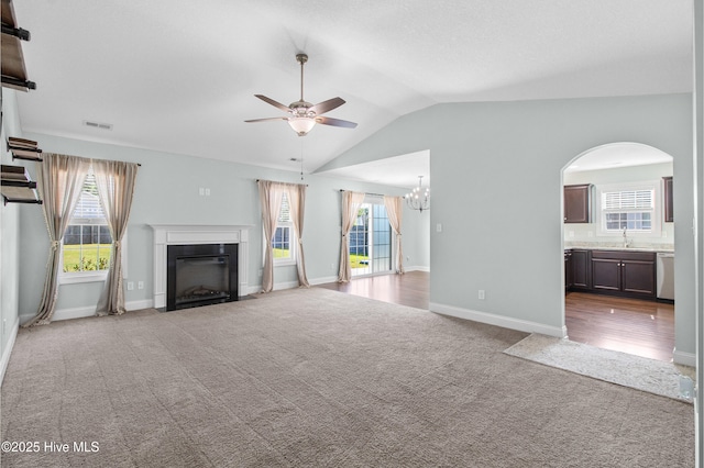 unfurnished living room with visible vents, carpet floors, a sink, ceiling fan with notable chandelier, and vaulted ceiling