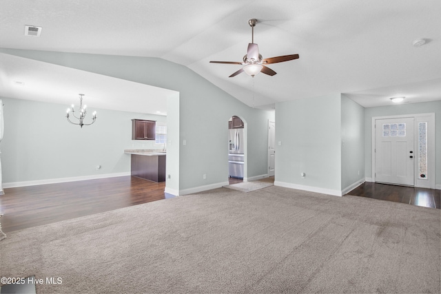 unfurnished living room featuring baseboards, vaulted ceiling, ceiling fan with notable chandelier, and dark colored carpet