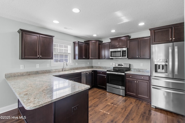 kitchen featuring dark brown cabinetry, a sink, a peninsula, stainless steel appliances, and dark wood-type flooring